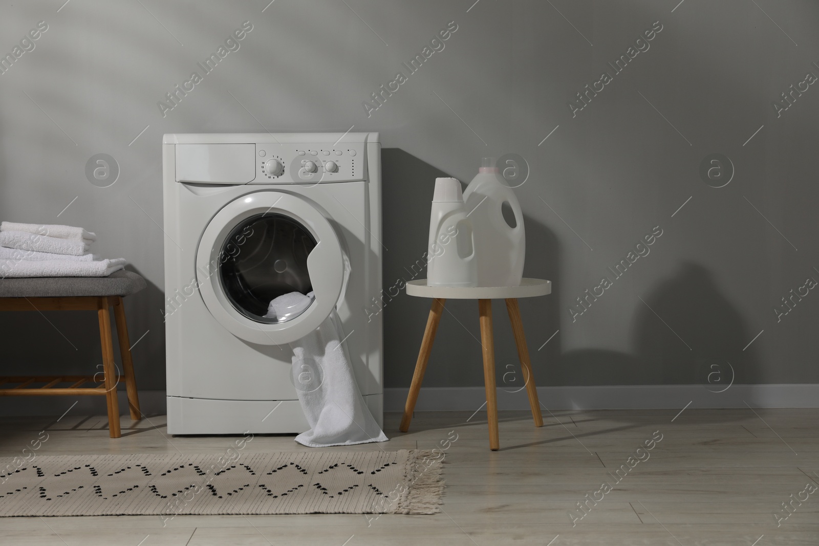 Photo of Washing machine, towels and detergents near grey wall