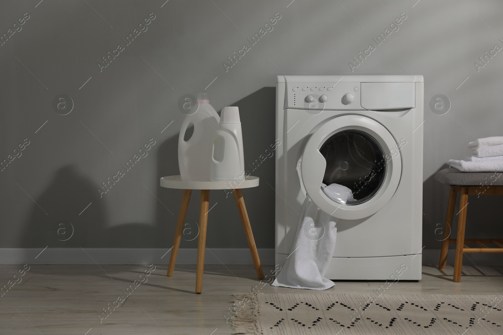 Photo of Washing machine, towels and detergents near grey wall