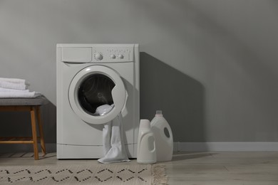 Photo of Washing machine, towels and detergents near grey wall, space for text