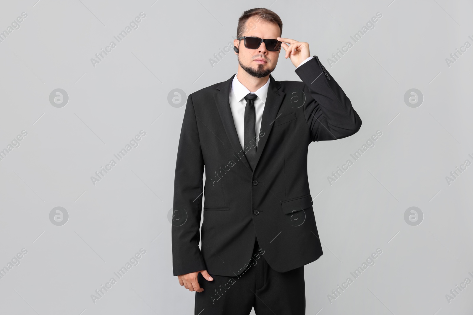 Photo of Young bodyguard in suit and sunglasses on grey background