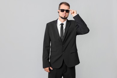 Young bodyguard in suit and sunglasses on grey background