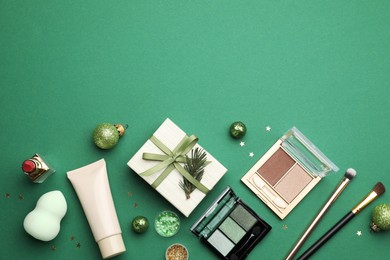 Flat lay composition with makeup products and Christmas decor on green background. Space for text