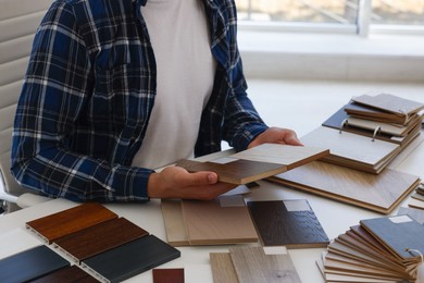 Photo of Man choosing wooden flooring among different samples at table, closeup