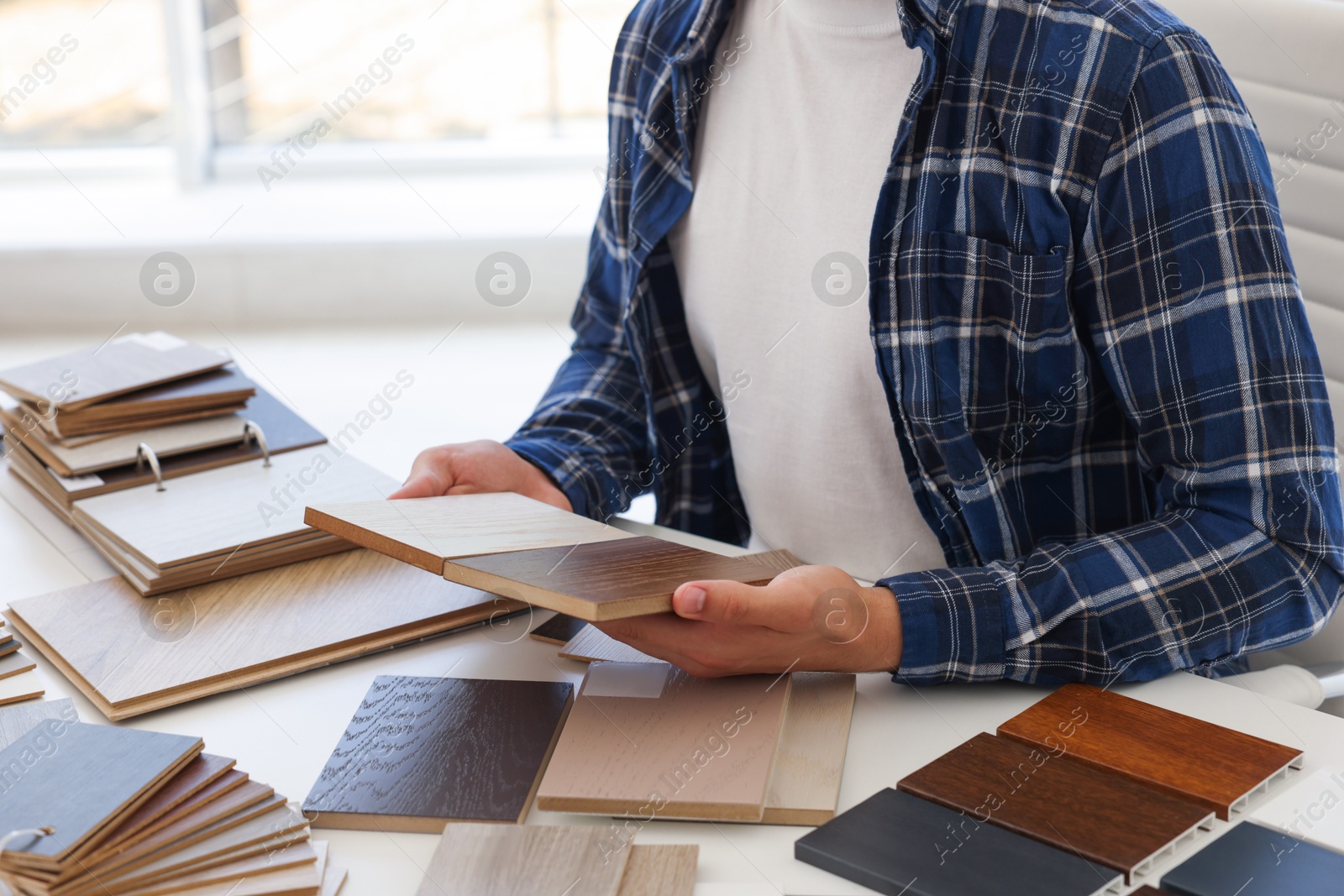 Photo of Man choosing wooden flooring among different samples at table, closeup