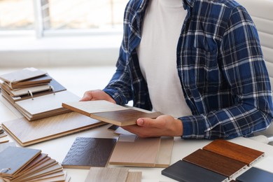 Photo of Man choosing wooden flooring among different samples at table, closeup