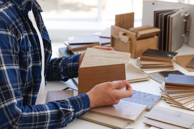 Photo of Man choosing wooden flooring among different samples at table, closeup