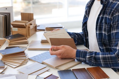 Photo of Man choosing wooden flooring among different samples at table, closeup