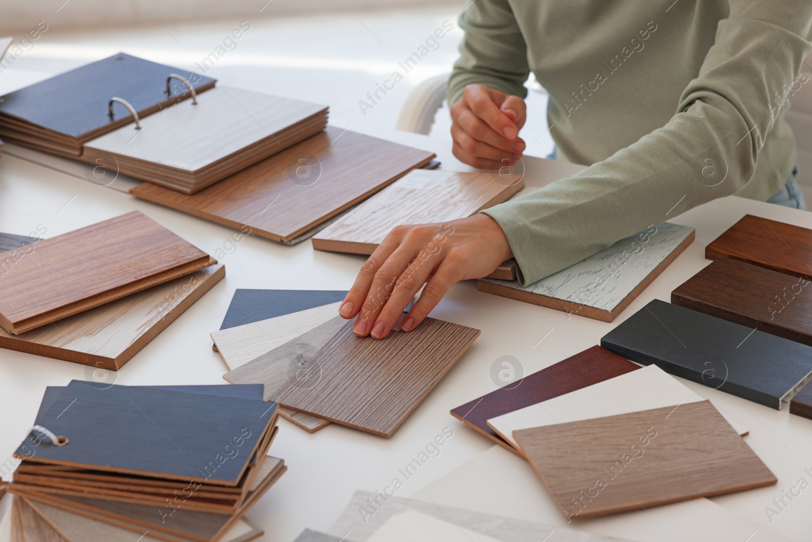 Photo of Woman choosing wooden flooring among different samples at table, closeup