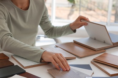 Photo of Woman choosing wooden flooring among different samples at table, closeup