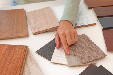 Photo of Woman choosing wooden flooring among different samples at table, closeup