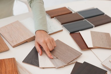 Photo of Woman choosing wooden flooring among different samples at table, closeup