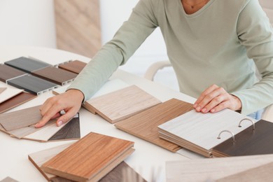 Photo of Woman choosing wooden flooring among different samples at table, closeup