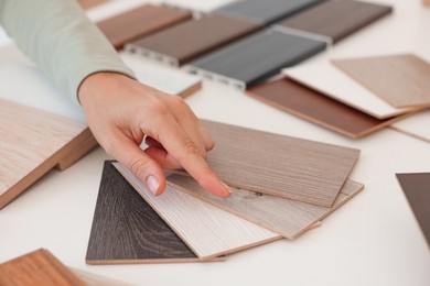 Photo of Woman choosing wooden flooring among different samples at table, closeup