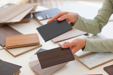 Photo of Woman choosing wooden flooring among different samples at table, closeup