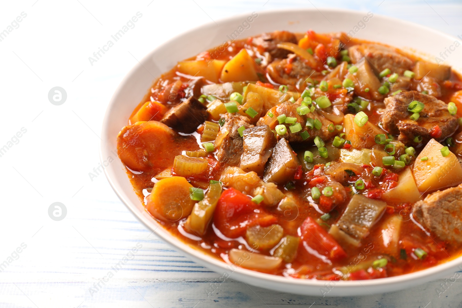 Photo of Delicious stew with vegetables in bowl on light blue wooden background, closeup