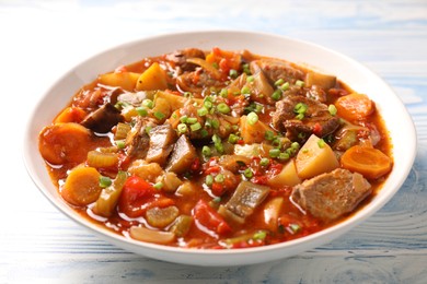 Delicious stew with vegetables in bowl on light blue wooden background, closeup