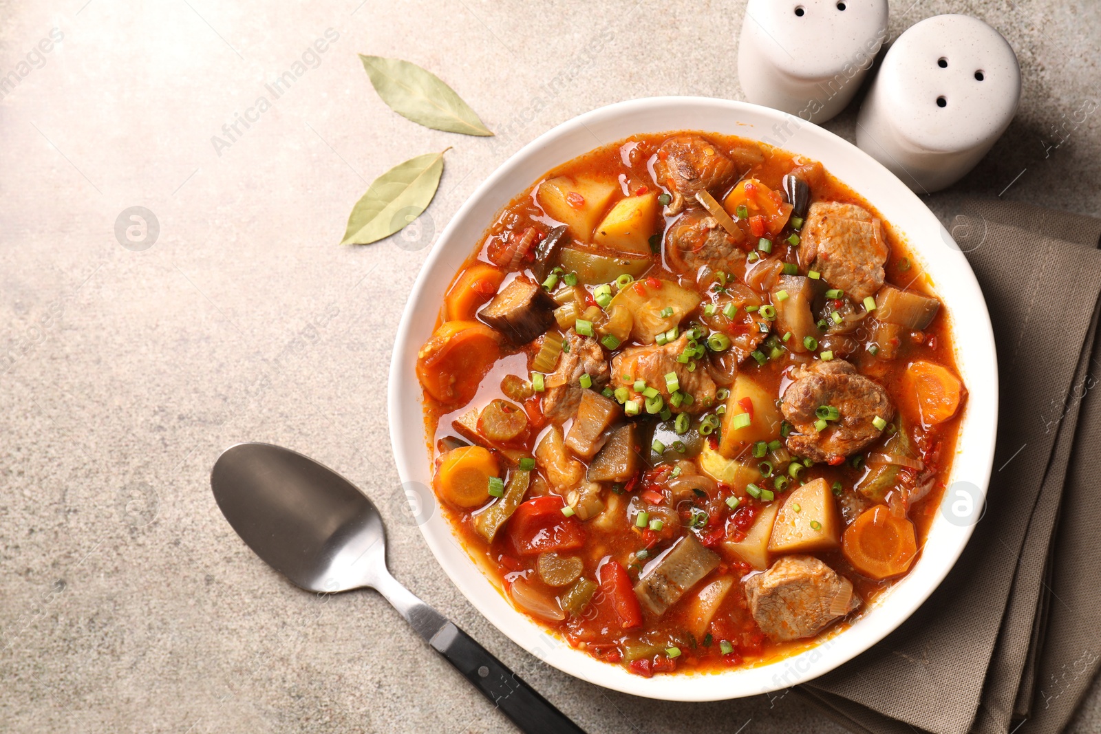 Photo of Delicious stew with vegetables in bowl, spices and spoon on light grey table, top view