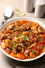 Delicious stew with vegetables in bowl on light grey table, closeup