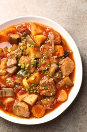 Delicious stew with vegetables in bowl on light grey table, top view