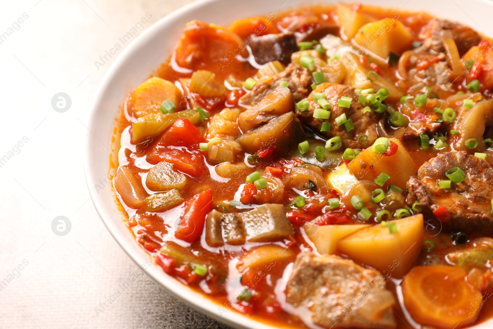 Photo of Delicious stew with vegetables in bowl on light grey table, closeup