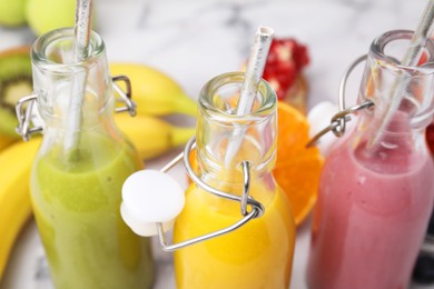 Glass bottles of tasty smoothies and different products on white marble table, closeup