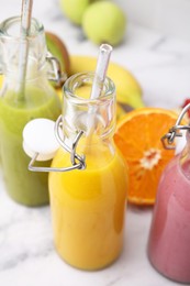 Glass bottles of tasty smoothies and different products on white marble table, closeup