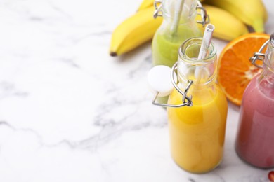 Photo of Glass bottles of tasty smoothies and different products on white marble table, closeup. Space for text