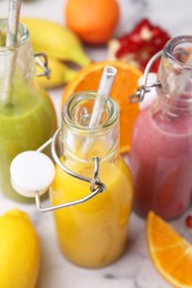 Photo of Glass bottles of tasty smoothies and different products on white marble table, closeup