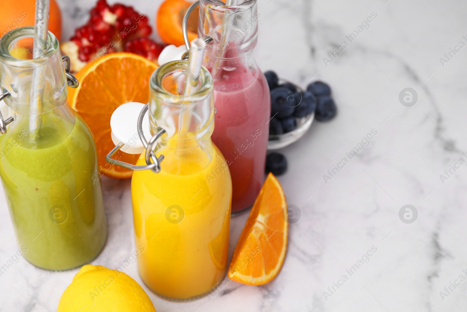 Photo of Glass bottles of tasty smoothies and different products on white marble table, closeup. Space for text