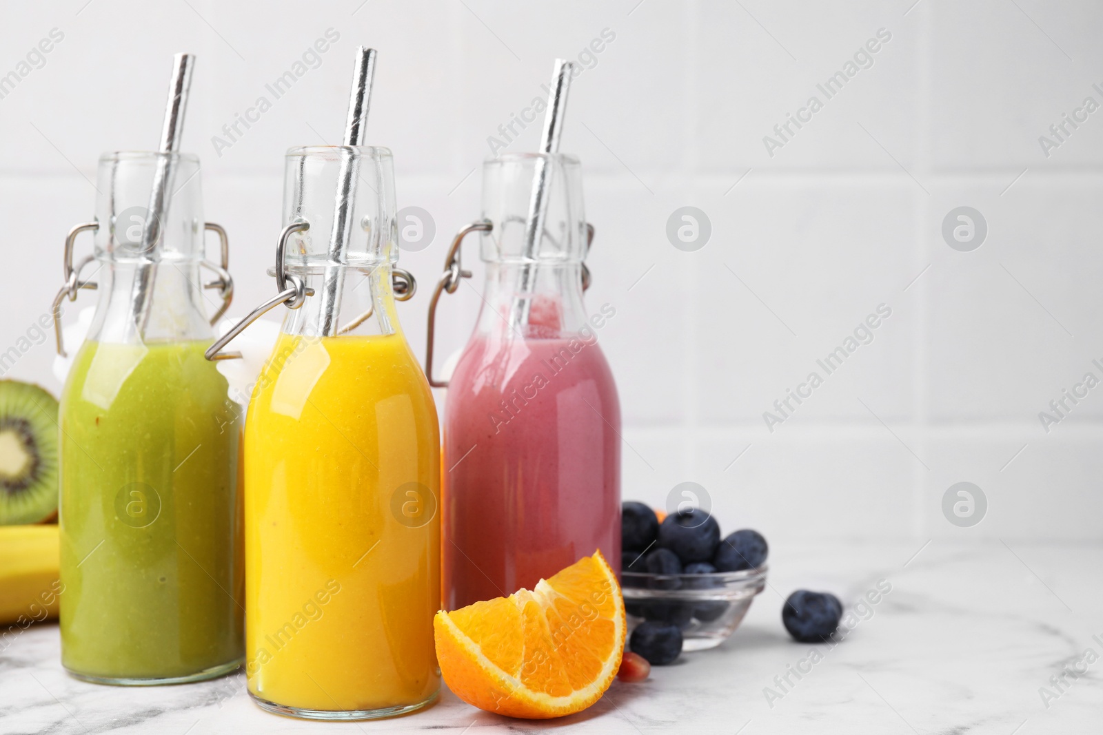 Photo of Glass bottles of tasty smoothies and different products on white marble table, space for text