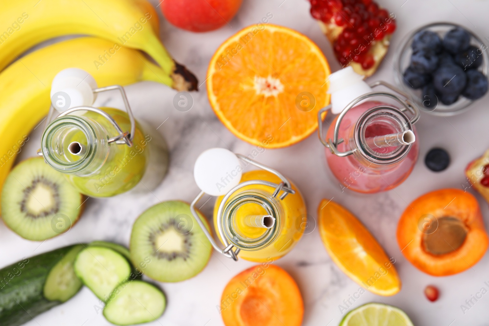 Photo of Glass bottles of tasty smoothies and different products on white marble table, flat lay