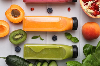 Photo of Glass bottles of tasty smoothies and different products on white tiled table, flat lay