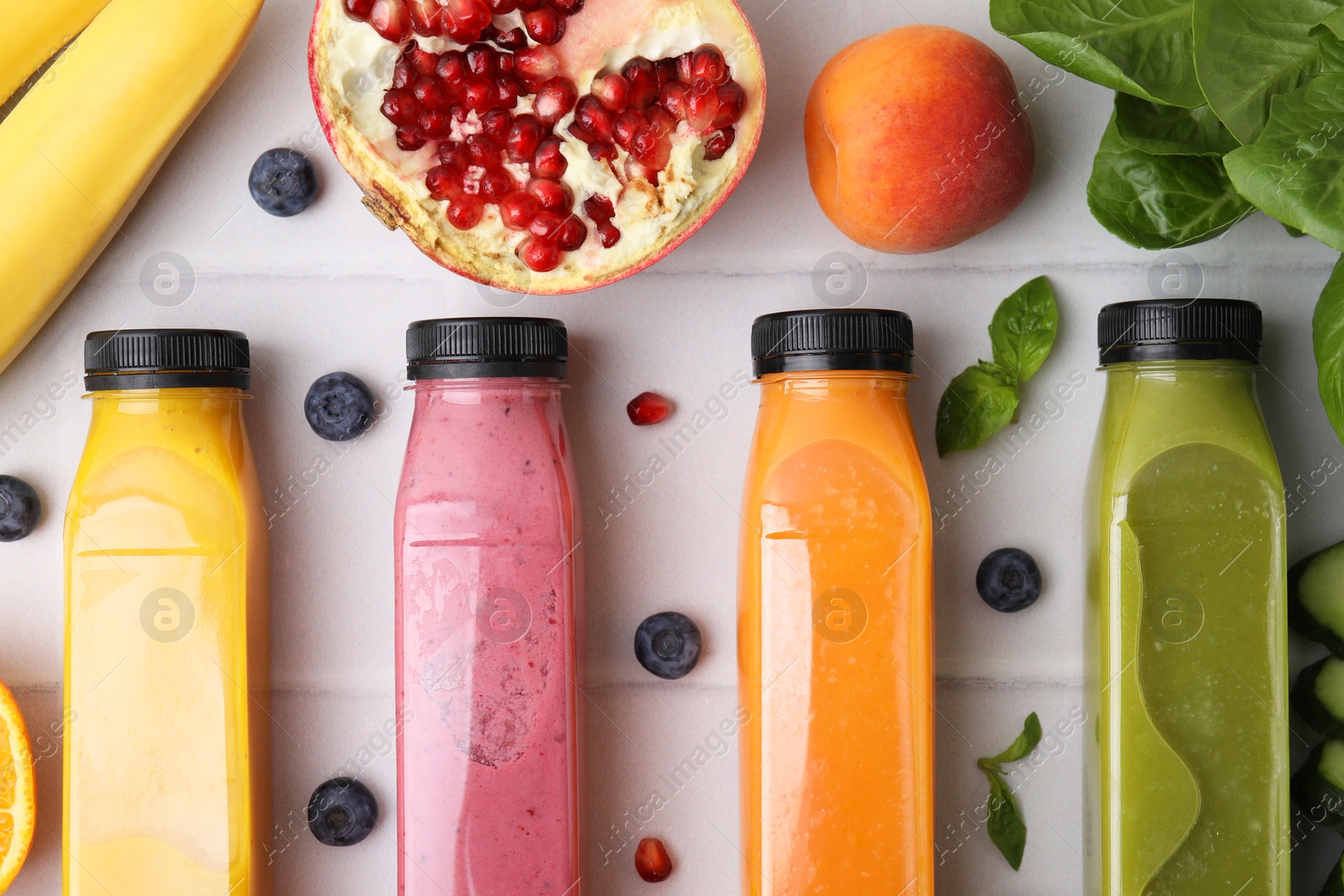 Photo of Glass bottles of tasty smoothies and different products on white tiled table, flat lay