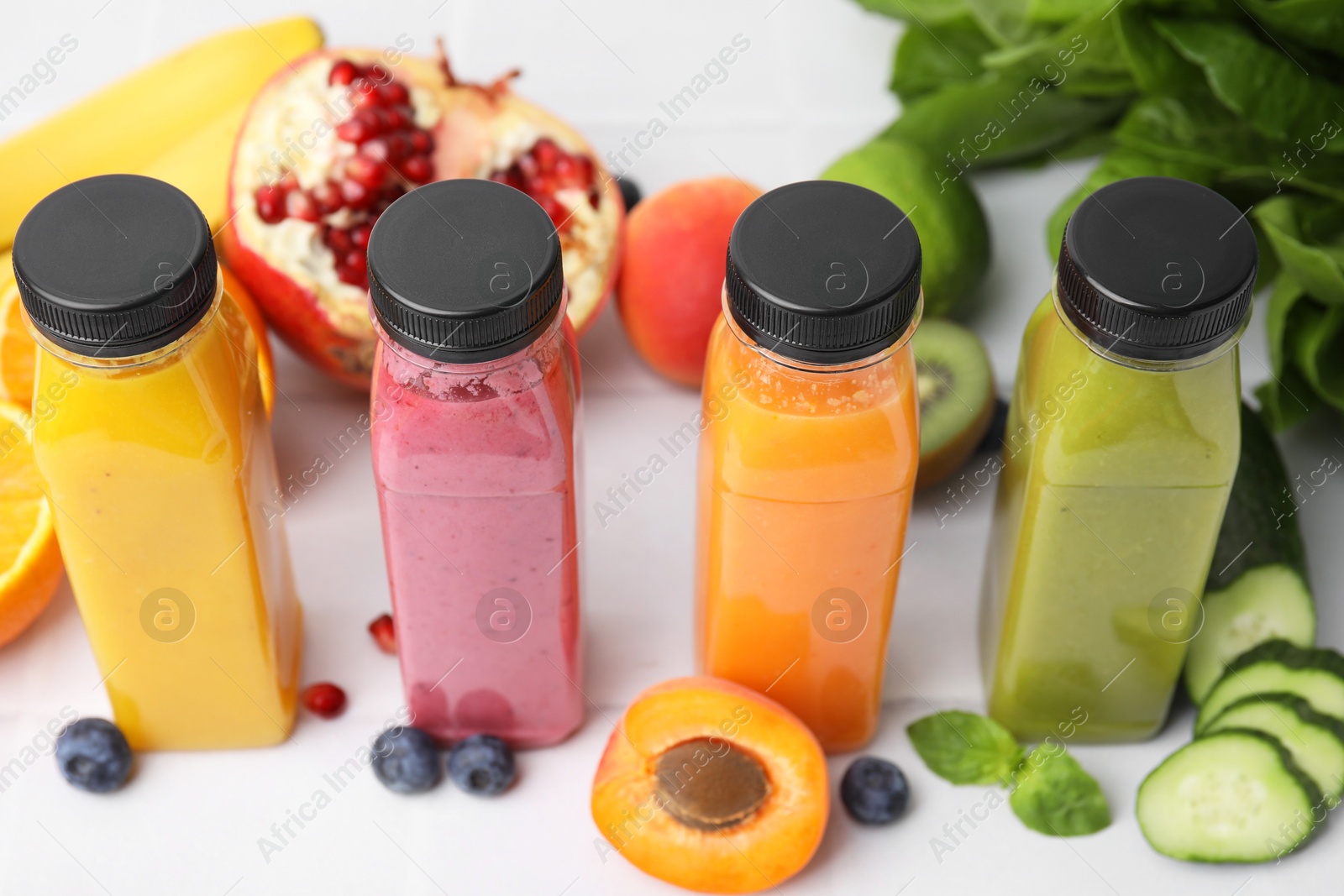 Photo of Glass bottles of tasty smoothies and different products on white tiled table