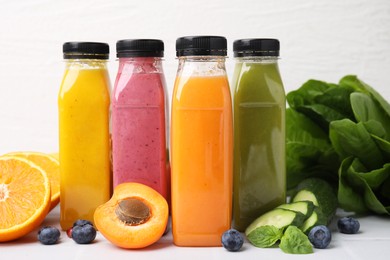 Glass bottles of tasty smoothies and different products on white tiled table