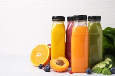 Glass bottles of tasty smoothies and different products on white tiled table, space for text