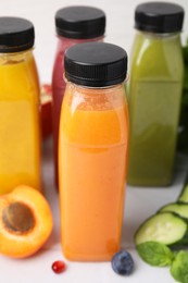 Glass bottles of tasty smoothies and different products on white tiled table, closeup