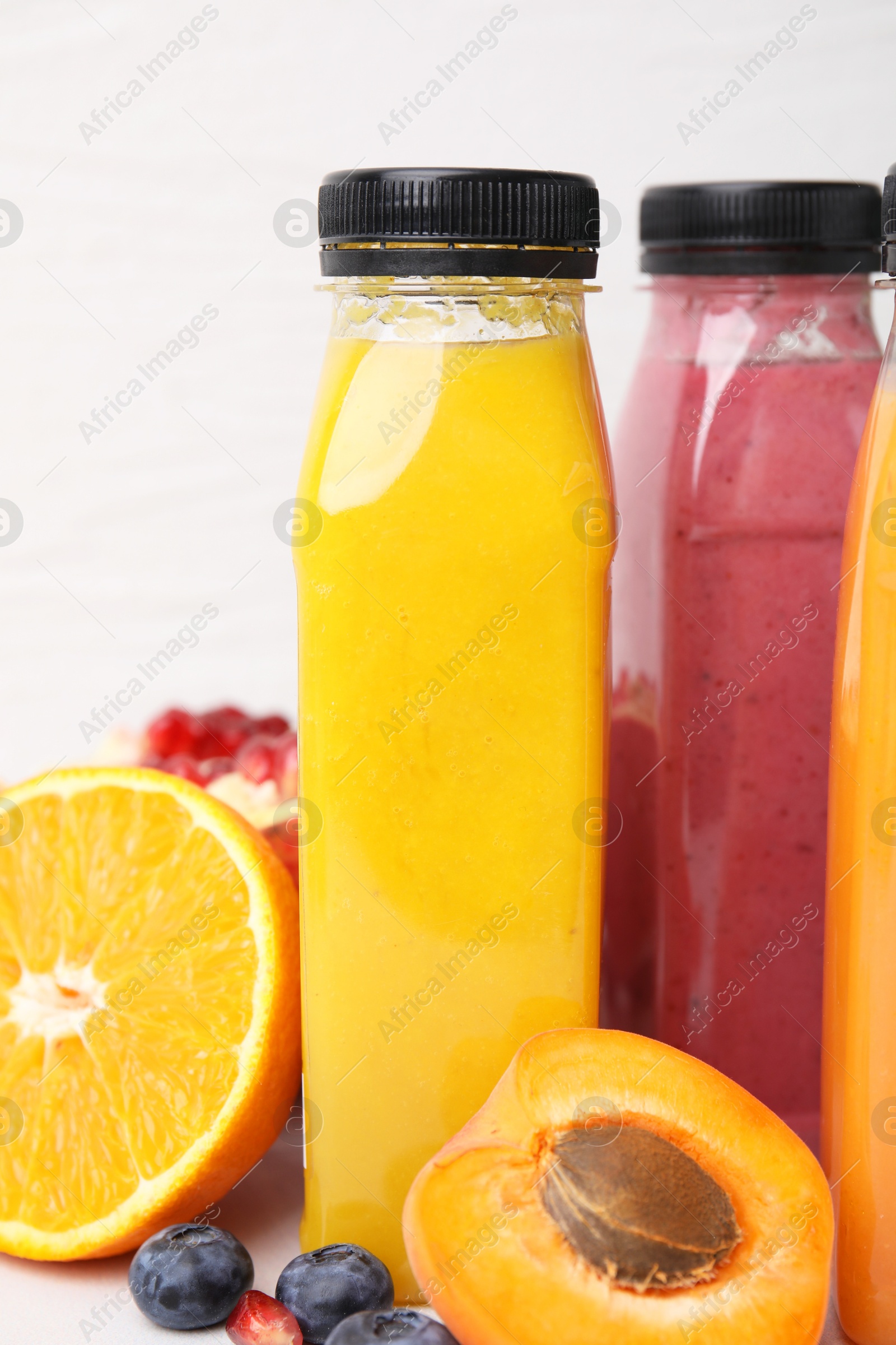 Photo of Glass bottles of tasty smoothies and different products on white tiled table, closeup