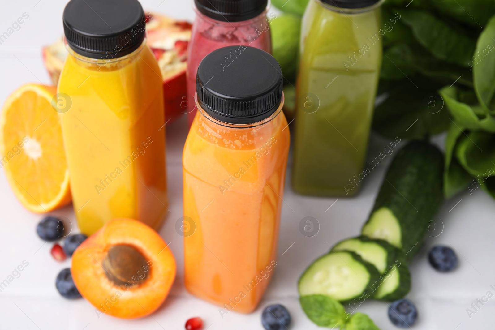 Photo of Glass bottles of tasty smoothies and different products on white tiled table, closeup