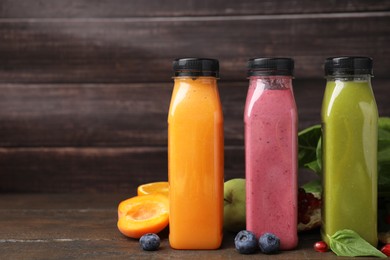 Glass bottles of tasty smoothies and different products on wooden table