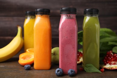 Glass bottles of tasty smoothies and different products on wooden table