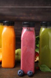 Glass bottles of tasty smoothies and different products on wooden table