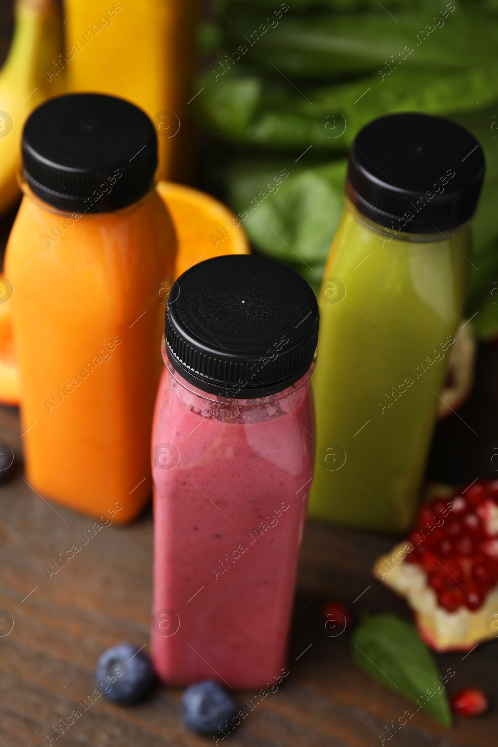 Photo of Glass bottles of tasty smoothies and different products on wooden table, closeup