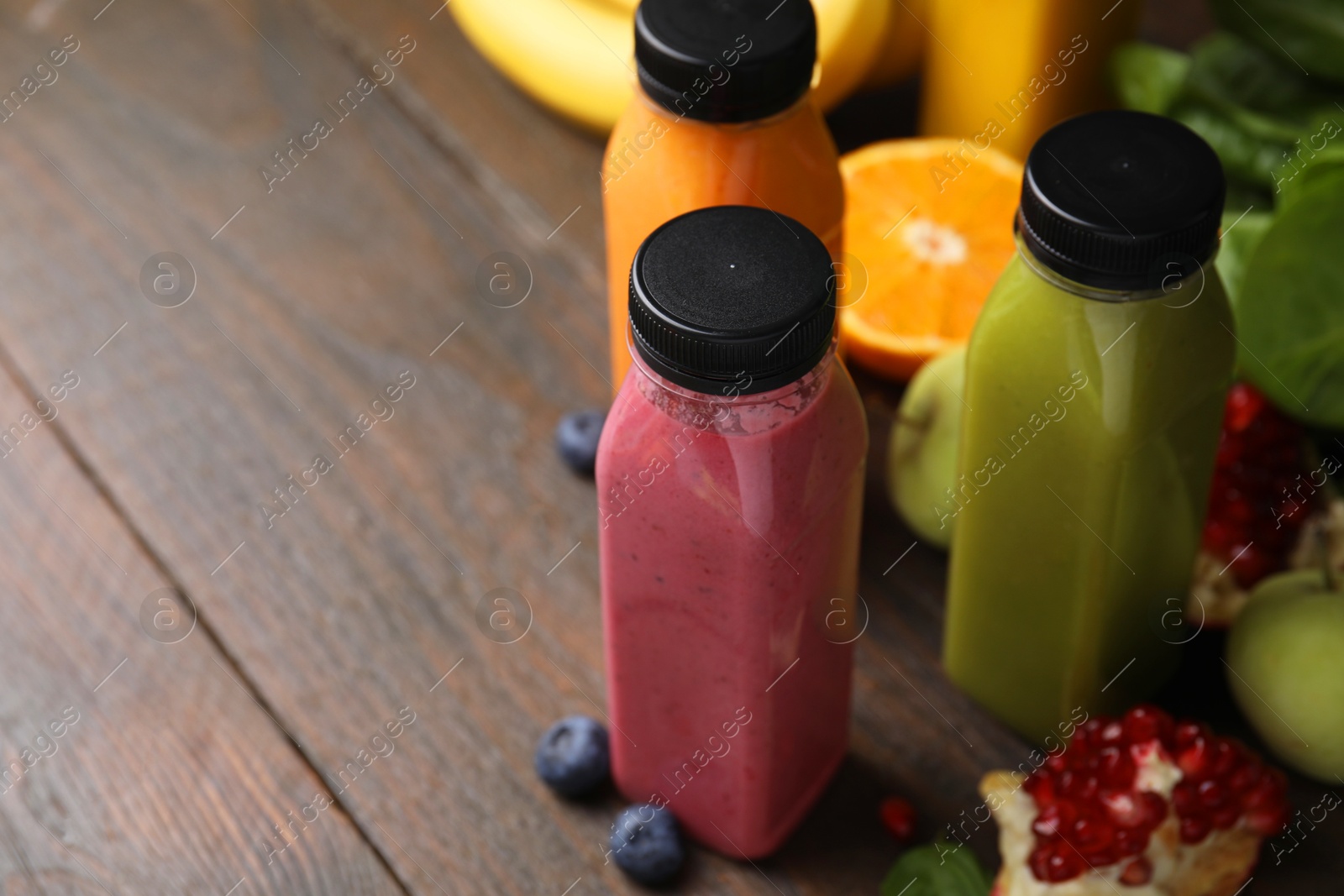 Photo of Glass bottles of tasty smoothies and different products on wooden table, closeup. Space for text