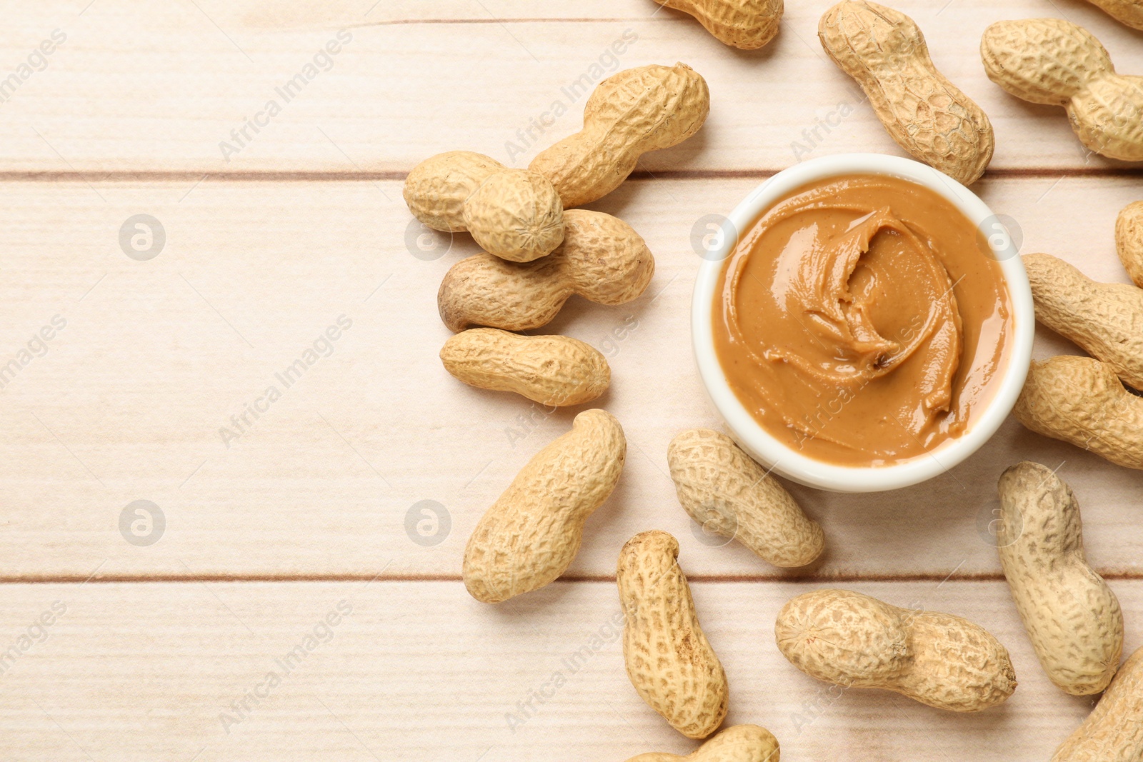 Photo of Tasty peanut butter in bowl and nuts on wooden table, flat lay. Space for text