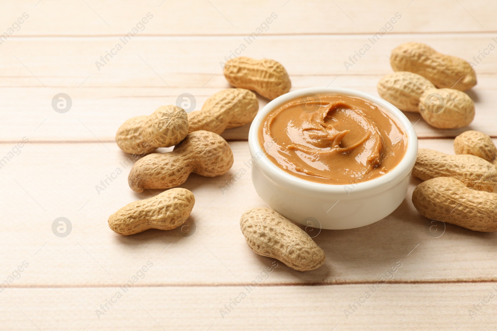 Photo of Tasty peanut butter in bowl and groundnuts on wooden table