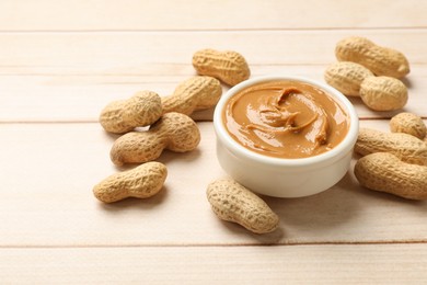 Photo of Tasty peanut butter in bowl and groundnuts on wooden table