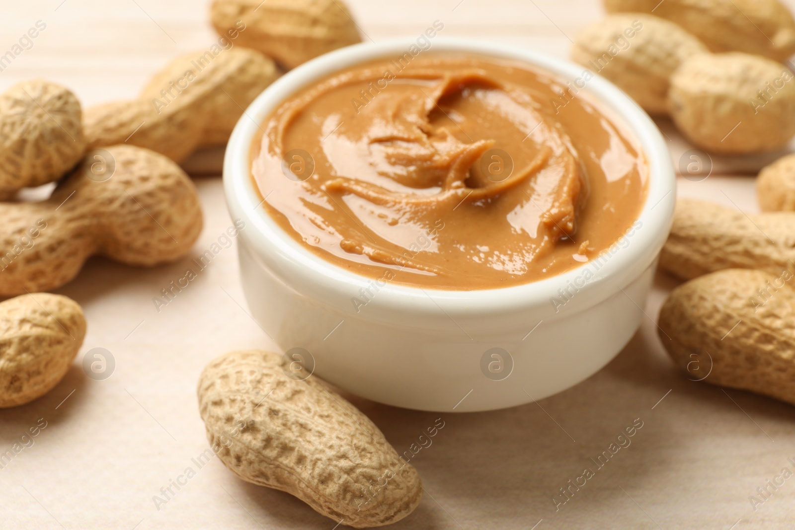 Photo of Tasty peanut butter in bowl and groundnuts on wooden table, closeup