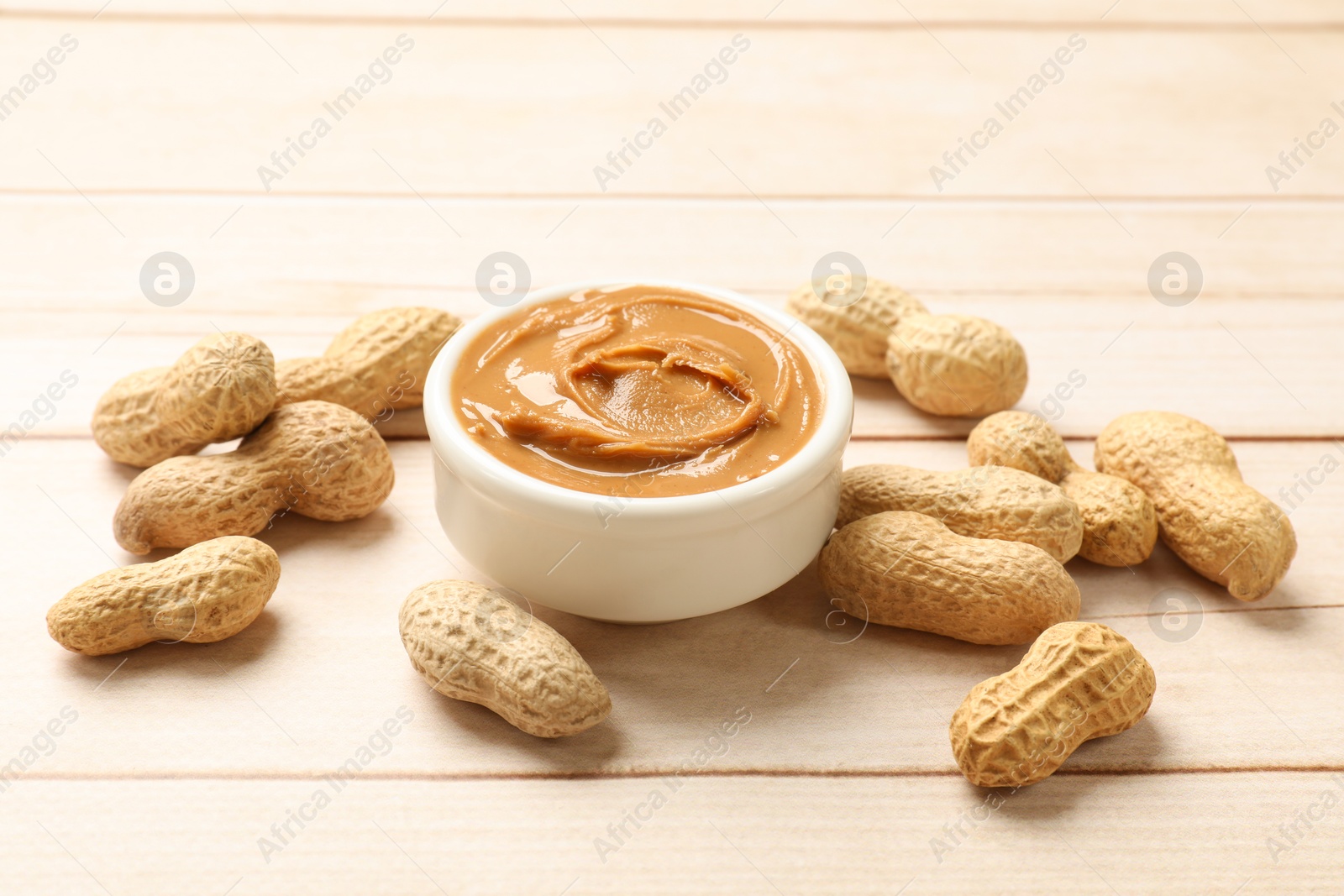 Photo of Tasty peanut butter in bowl and groundnuts on wooden table