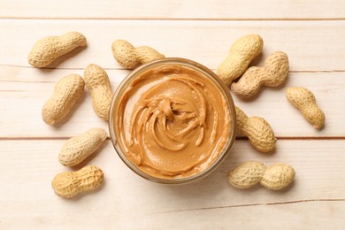 Photo of Tasty peanut butter in bowl and nuts on wooden table, flat lay